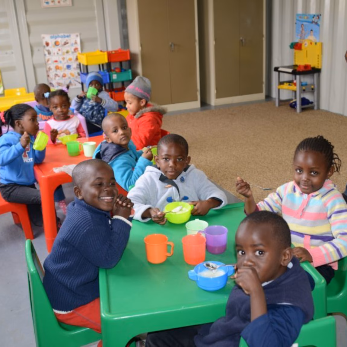 Kinderen nemen deel aan een gezamenlijke eet- of opvangactiviteit in een binnenruimte.