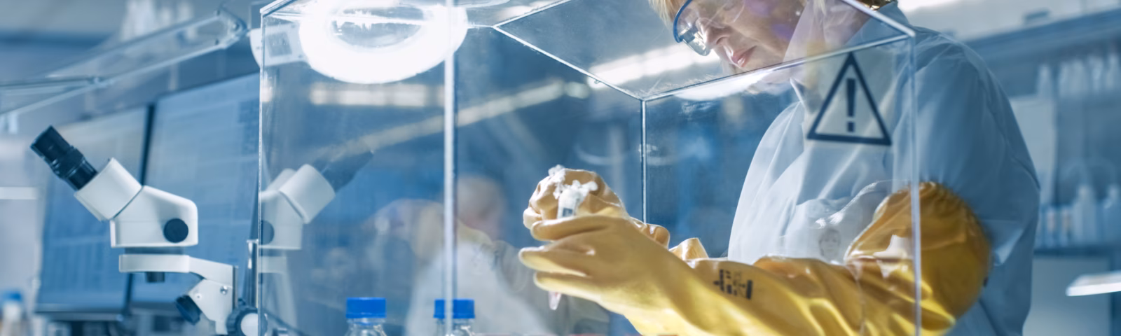 A laboratory technician examines samples in a sterile test environment using test tubes and laboratory equipment.