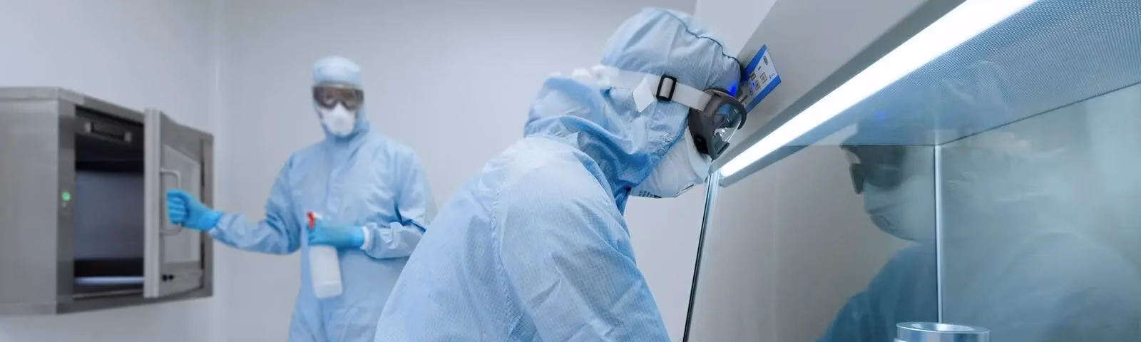 Employees wearing cleanroom suits perform quality control and sample processing in a sterile laboratory environment.