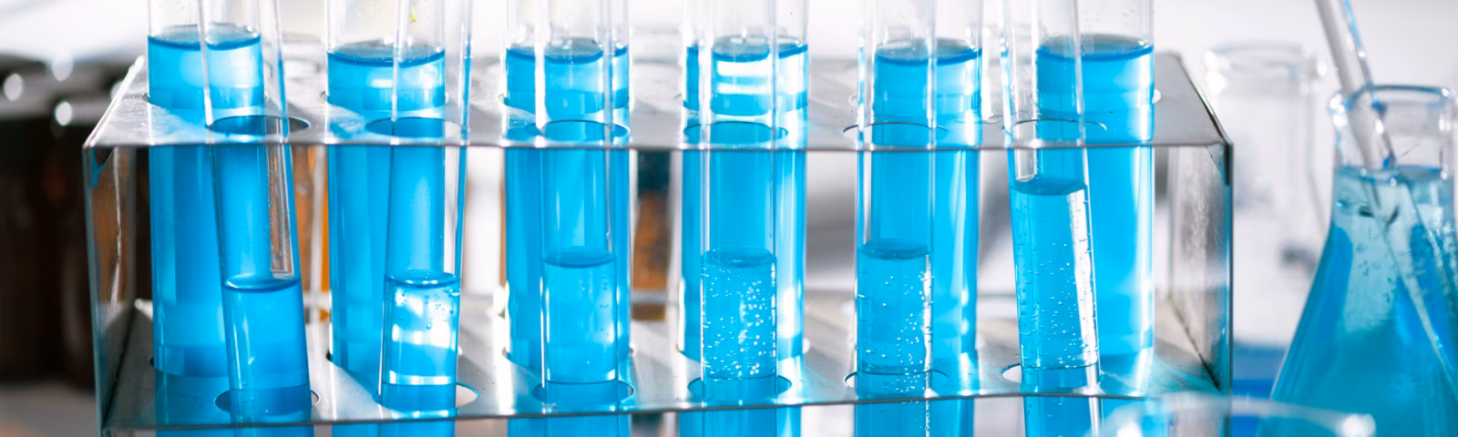 Test tubes filled with a blue liquid arranged in a laboratory for chemical analysis or quality testing.
