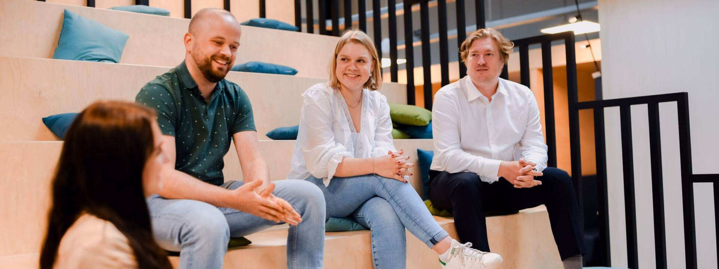A group discussion among four professionals in a modern office setting with wooden bleacher seating.