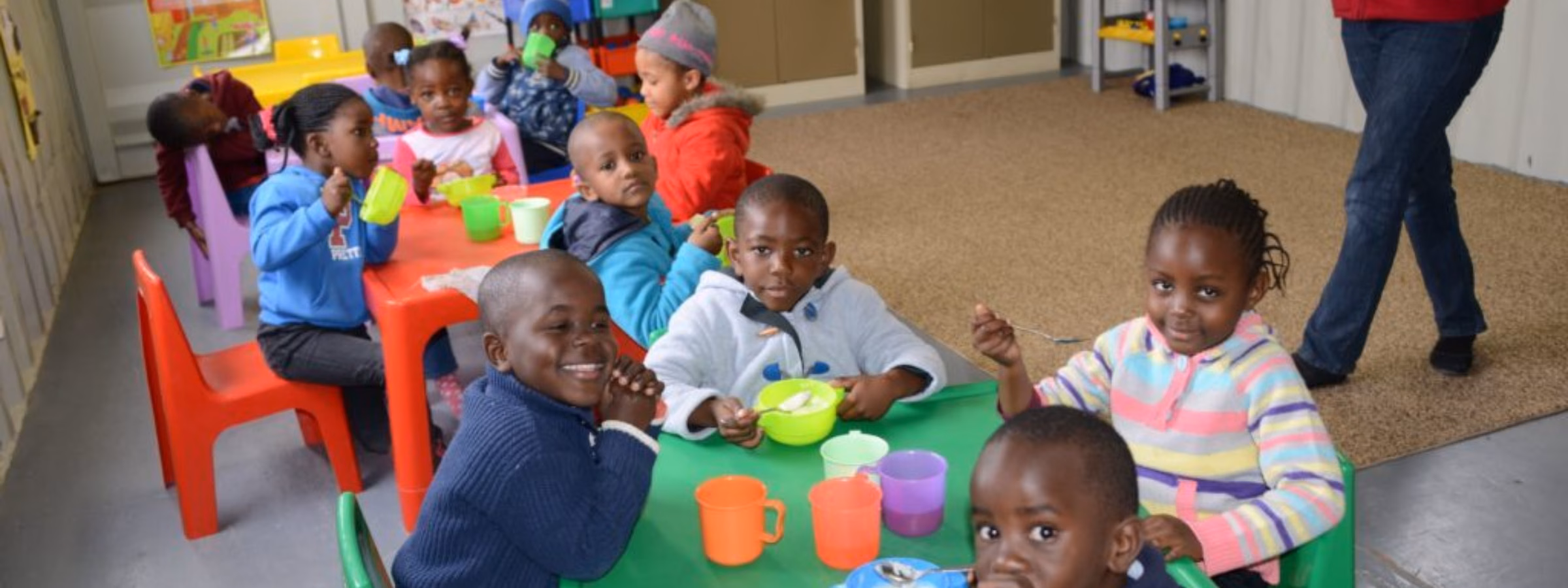 Kinderen nemen deel aan een gezamenlijke eet- of opvangactiviteit in een binnenruimte.