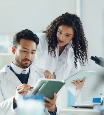 Science, talking and people on tablet in lab with microscope for analysis, medical research and study. Biology, pharmaceutical team and man with woman on tech for results, review and online report.