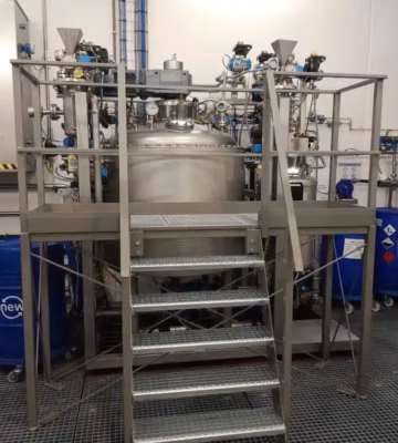 Prozessanlage aus Edelstahl mit Mischbehälter, Rohrleitungen und Plattform in einer industriellen Produktionsumgebung.
