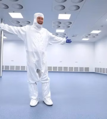 Person in Reinraumkleidung mit ausgestreckten Armen in einem sterilen Produktionsraum.