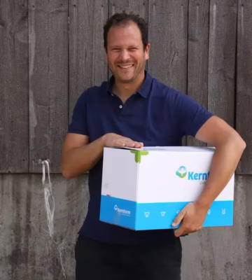 Eine Person hält einen weiß-blauen Karton vor einer Holzwand.