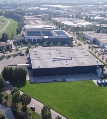 Luftaufnahme eines modernen Gewerbe- oder Distributionskomplexes mit mehreren Werkshallen, grünen Rasenflächen und umliegenden Straßen.