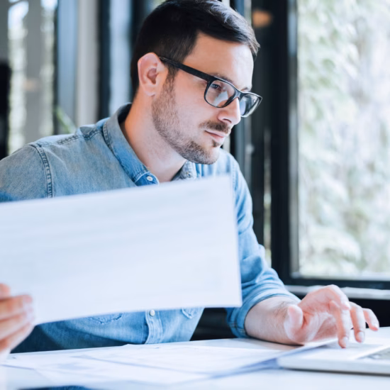 Persoon werkt aan een laptop en bekijkt een document in een moderne kantooromgeving.