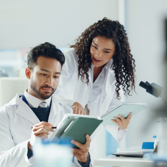 Science, talking and people on tablet in lab with microscope for analysis, medical research and study. Biology, pharmaceutical team and man with woman on tech for results, review and online report.