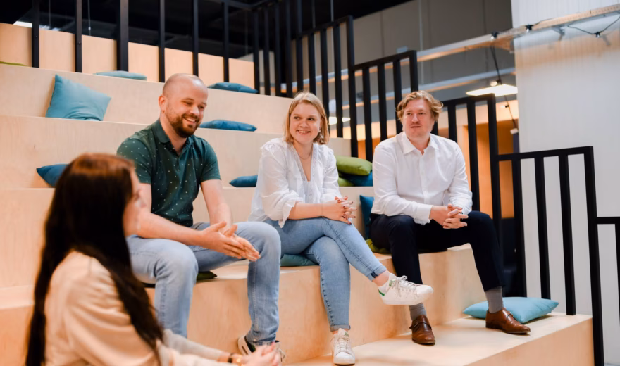 Groepsgesprek tussen vier professionals in een moderne kantooromgeving met houten tribunezittingen.