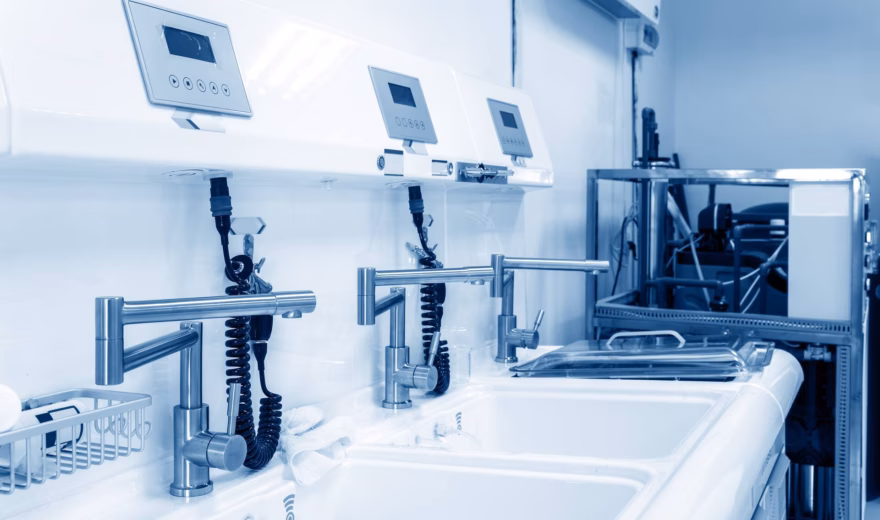 Steriele wasruimte met medische wastafels, dispensers en monitoringapparatuur voor hygiëne in een zorgomgeving.