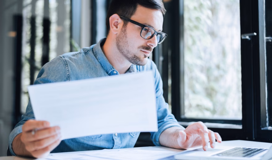 Persoon werkt aan een laptop en bekijkt een document in een moderne kantooromgeving.