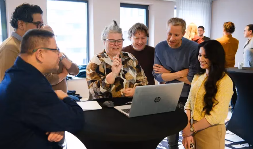Groep professionals bespreekt informatie rond een laptop tijdens een bijeenkomst op kantoor.