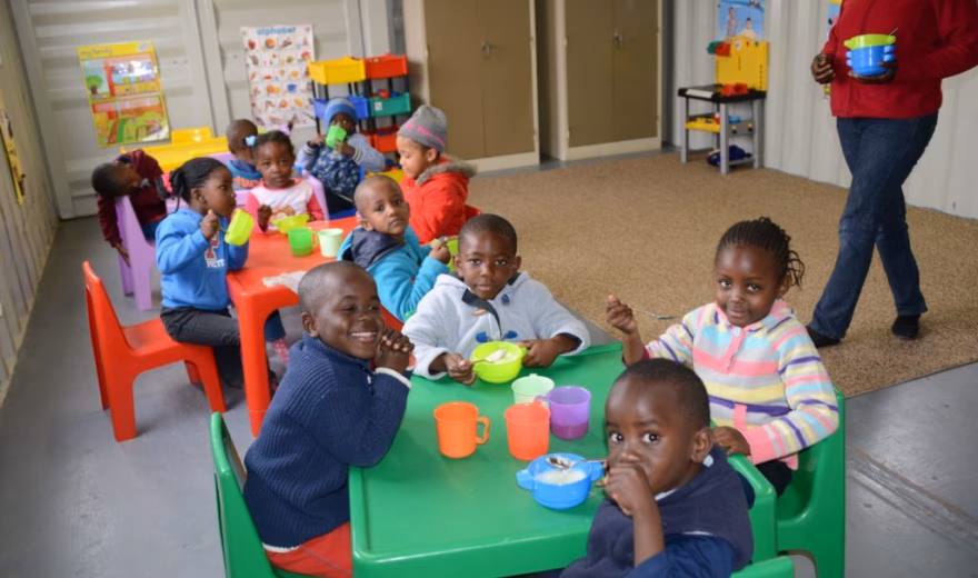 Kinderen nemen deel aan een gezamenlijke eet- of opvangactiviteit in een binnenruimte.