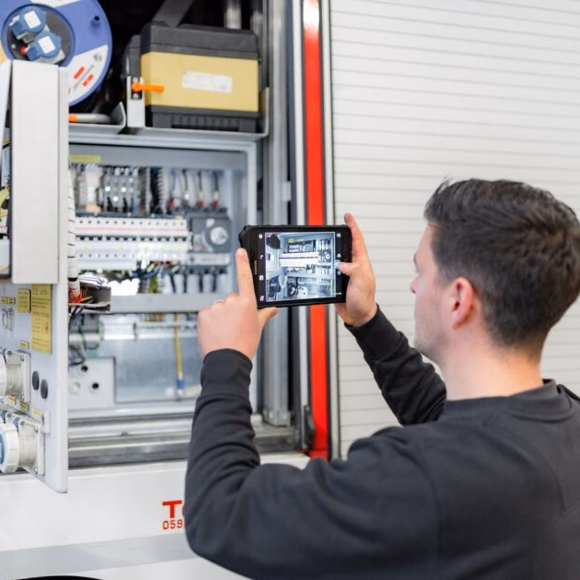 Technicus inspecteert een elektrische schakelkast met een tablet tijdens een technische installatiecontrole.