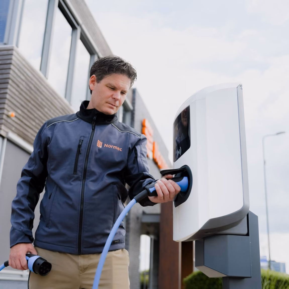 Une personne recharge une voiture électrique à une borne de recharge située à côté d'une habitation.