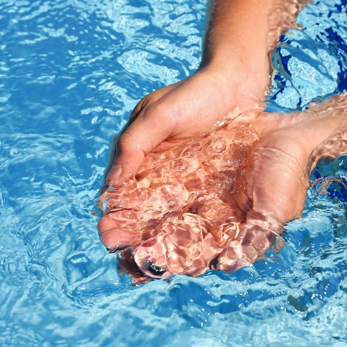 Hands scooping clear water from a swimming pool as a symbol of water quality and clean swimming water.