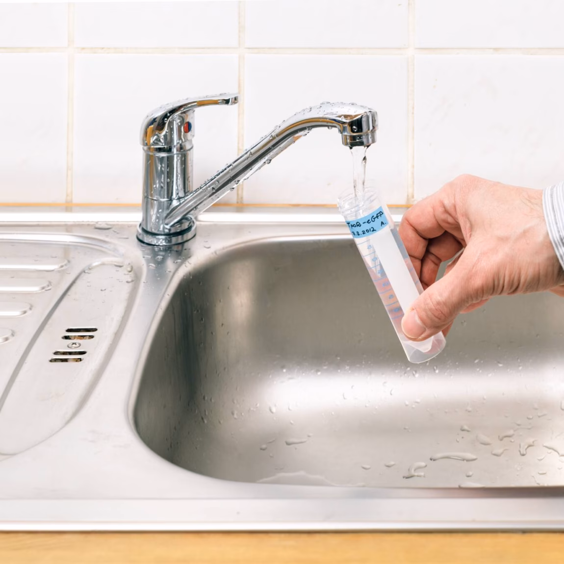 A water sample is collected from a kitchen faucet above a stainless steel sink.