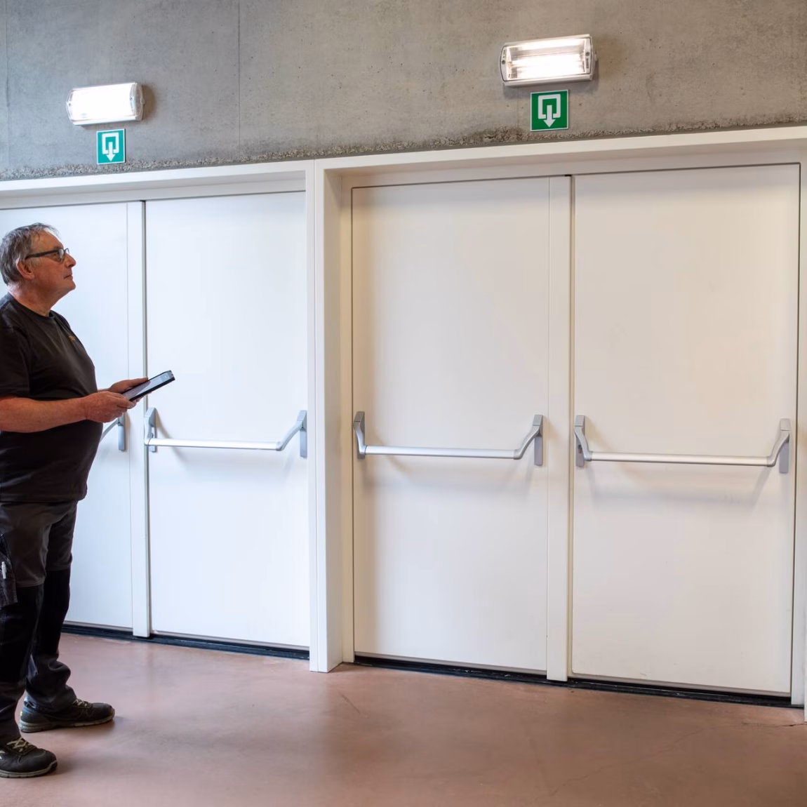 Inspecteur controleert nooddeuren en vluchtwegen in een gebouw met behulp van een tablet.
