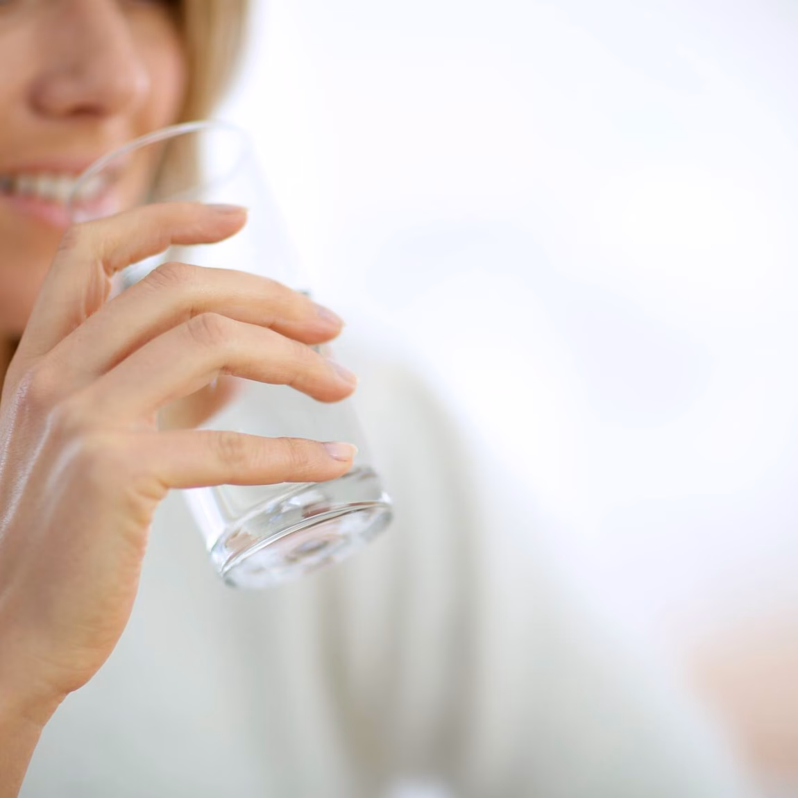 Une personne boit un verre d'eau dans un intérieur lumineux.