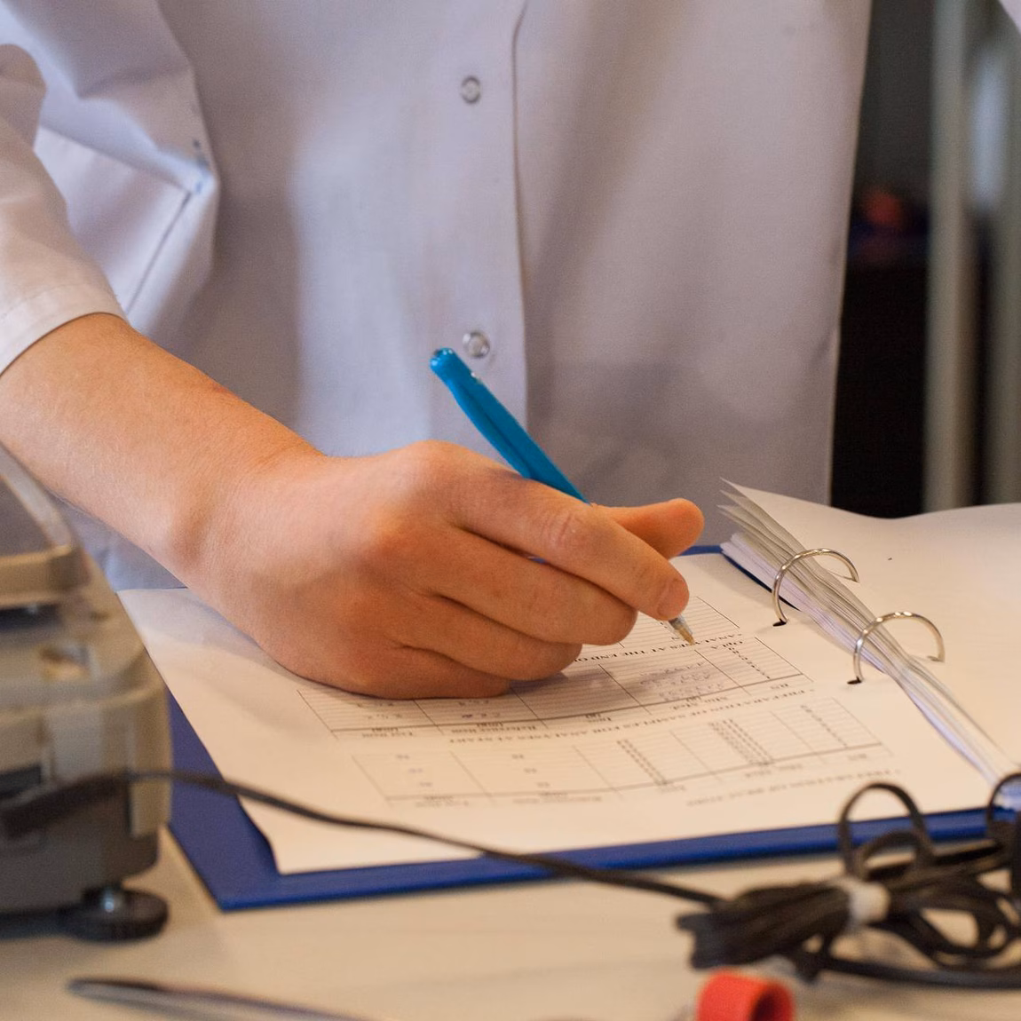 Une personne en blouse de laboratoire note des données de mesure sur un formulaire à côté d'un équipement de laboratoire.