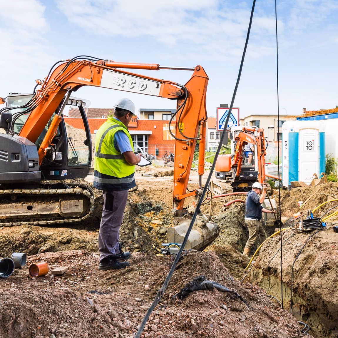 A technician supervises excavation work at a construction site involving excavators and underground infrastructure.