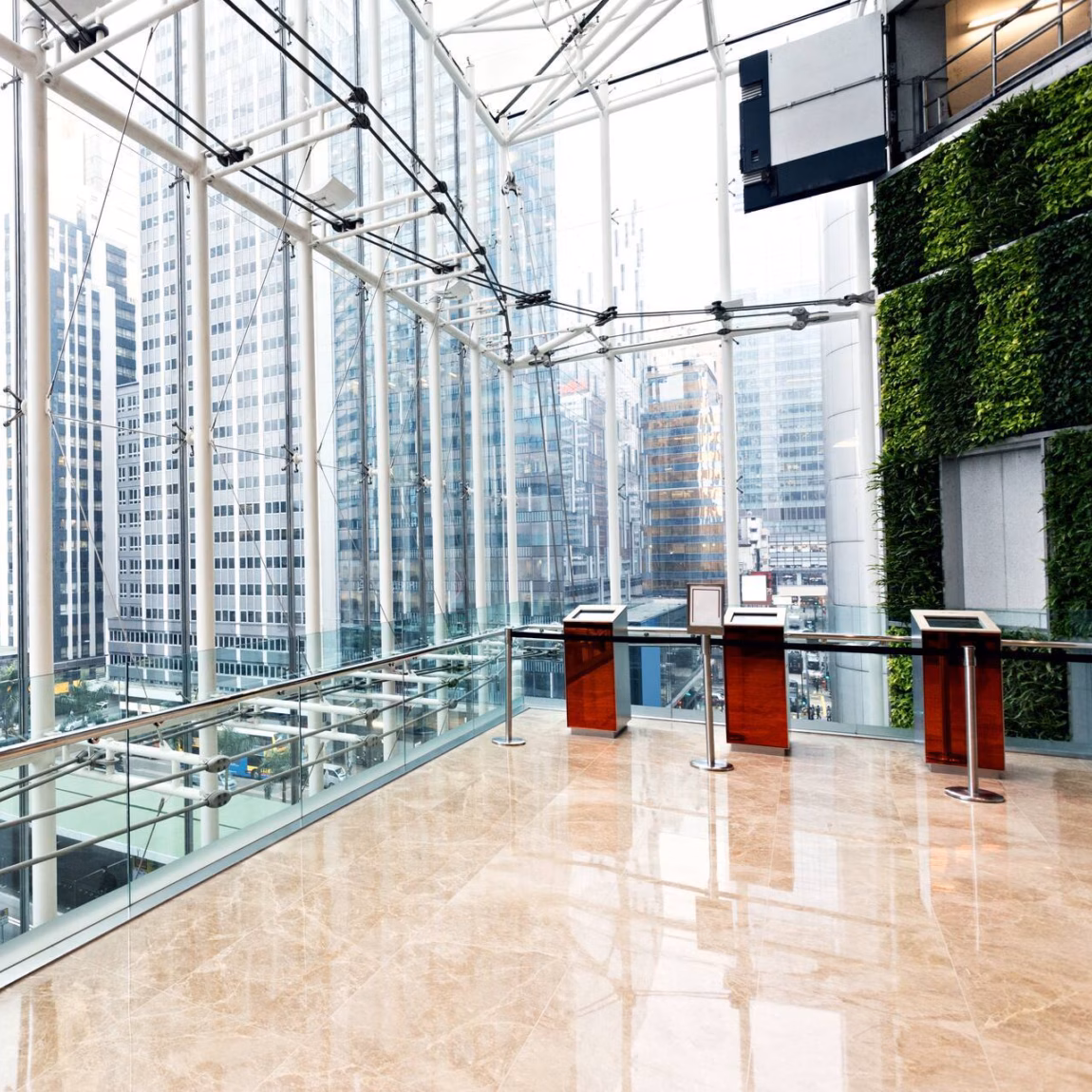 Moderne, verglaste Büro-Lobby mit Blick auf Hochhäuser und viel Tageslicht.