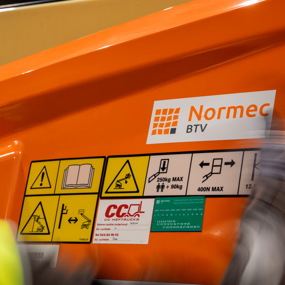 Detailfoto van veiligheidsstickers en Normec BTV-markering op een hoogwerker.