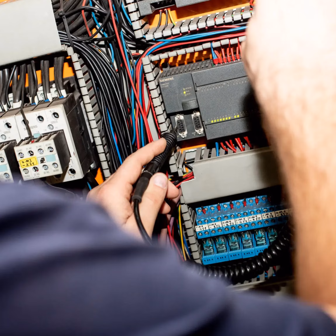 Ein Techniker führt Messungen in einem geöffneten Schaltschrank mit Verkabelung und Komponenten durch.