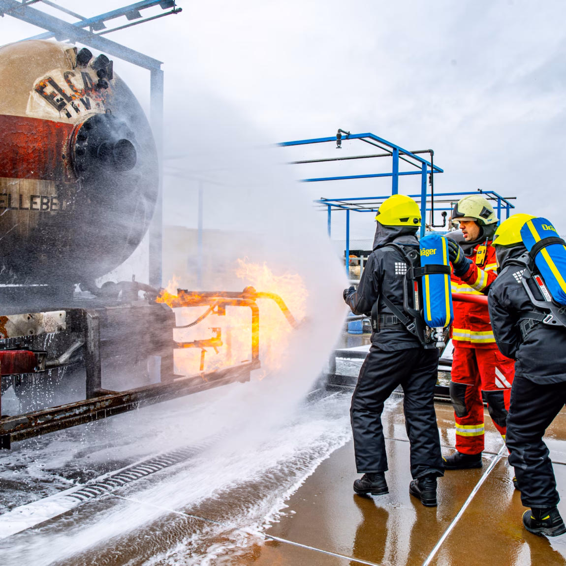 Einsatzkräfte bekämpfen bei einem Vorfall auf einem Außengelände einen Brand mit Schaum und Wasser.