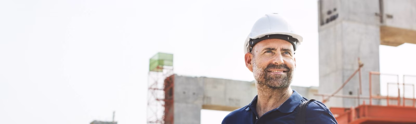 Eine Person mit Schutzhelm hält Dokumente auf einer im Bau befindlichen Baustelle in der Hand.