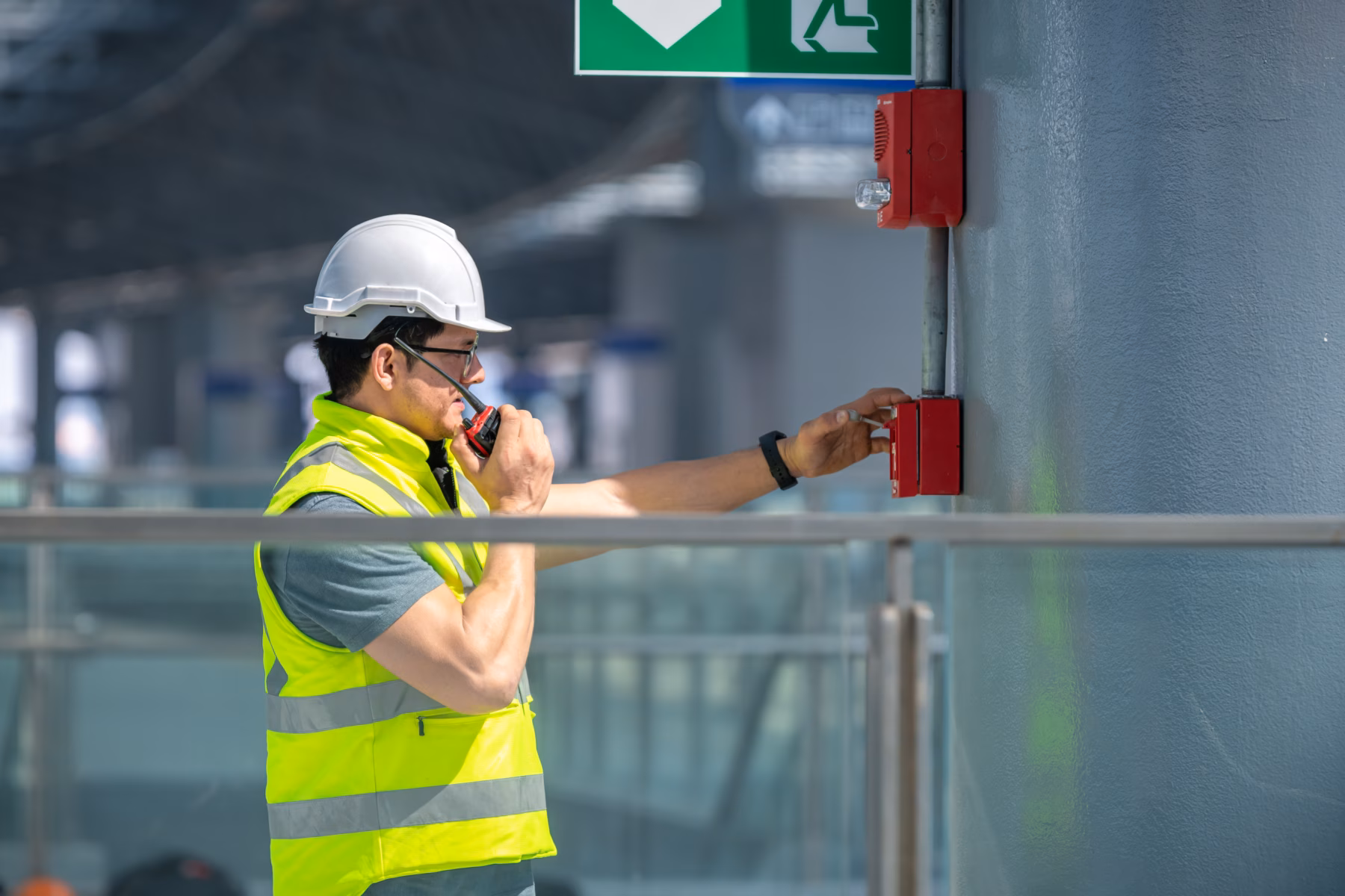 Normec technician wearing a white safety helmet and a high-visibility vest while inspecting fire safety systems in a commercial building.