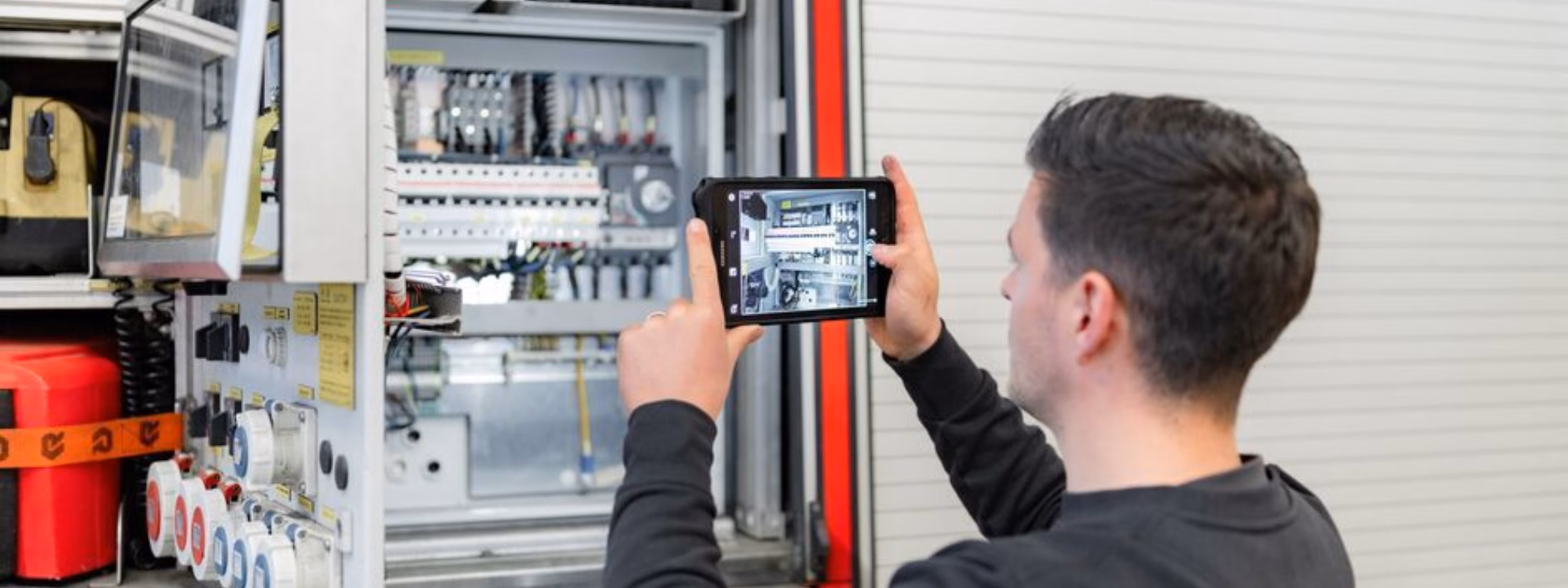 Technicus inspecteert een elektrische schakelkast met een tablet tijdens een technische installatiecontrole.