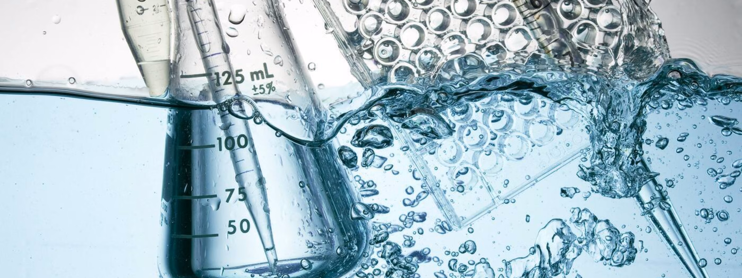 Verrerie de laboratoire comprenant des éprouvettes graduées, des pipettes et des plaques de réaction immergées, visibles dans un environnement de test ou d'analyse.