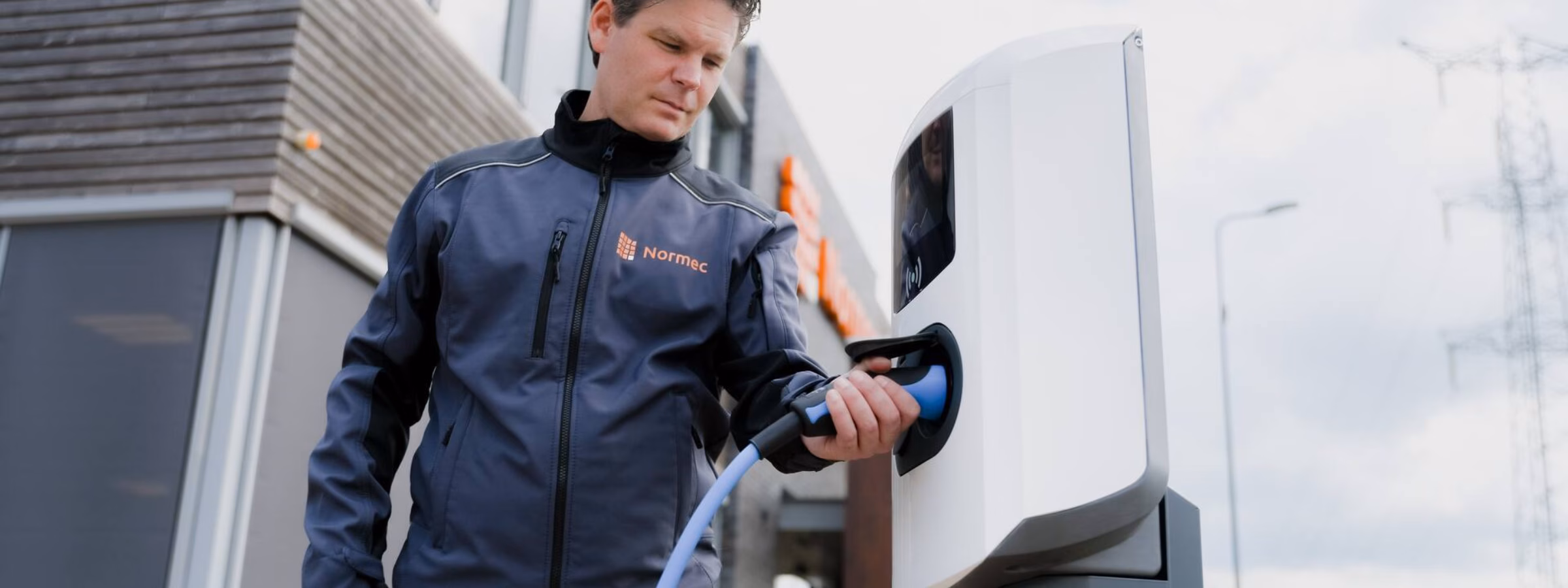 Une personne recharge une voiture électrique à une borne de recharge située à côté d'une habitation.