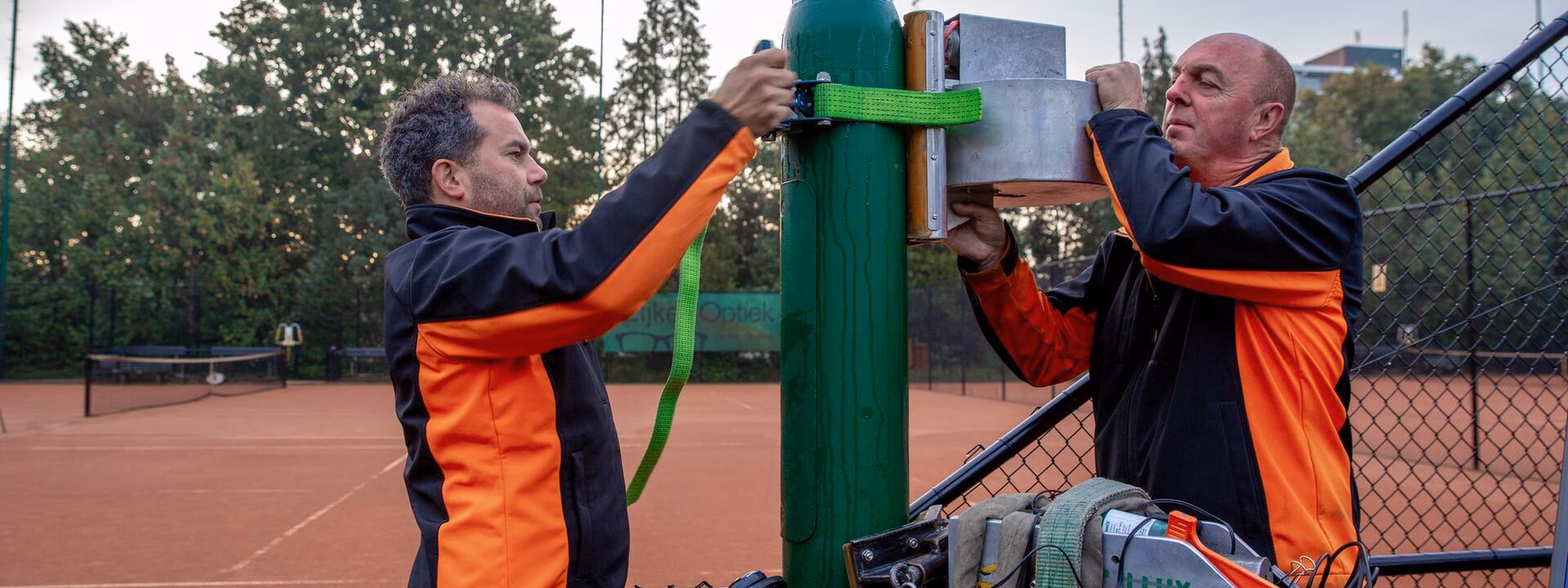 Des employés inspectent un mât d'éclairage sur un terrain de sport à l'aide d'une nacelle élévatrice.