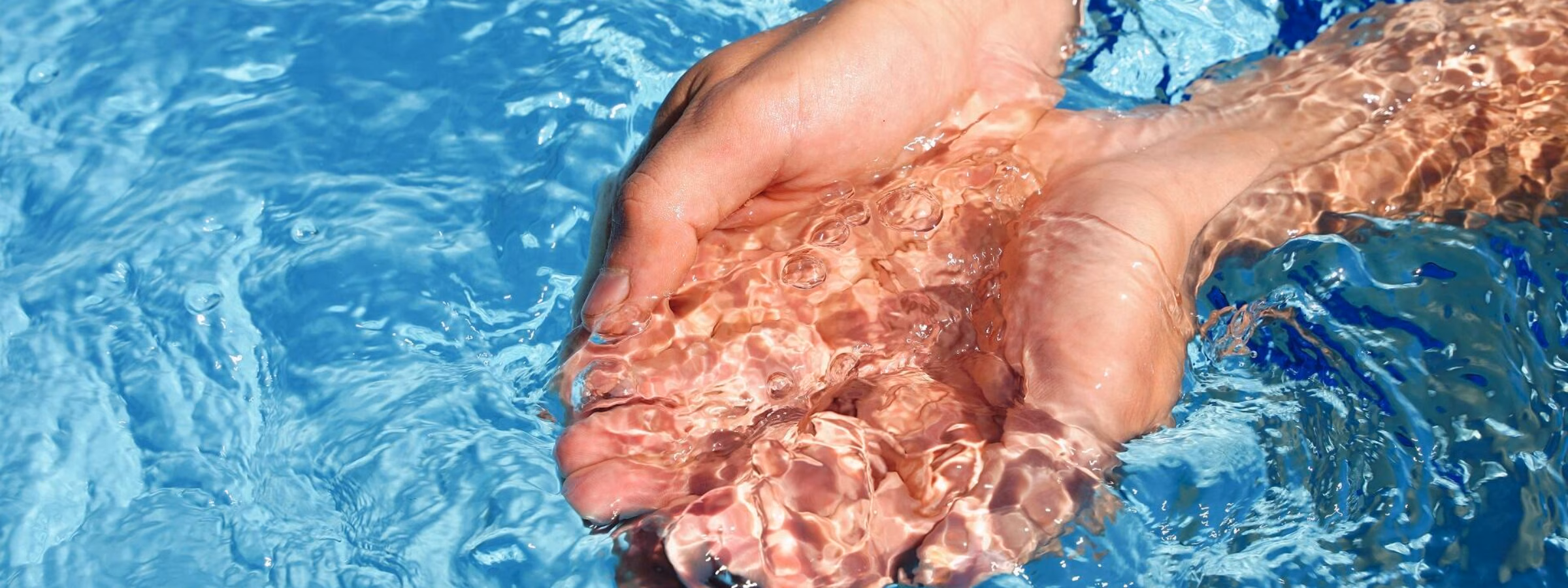 Hands scooping clear water from a swimming pool as a symbol of water quality and clean swimming water.