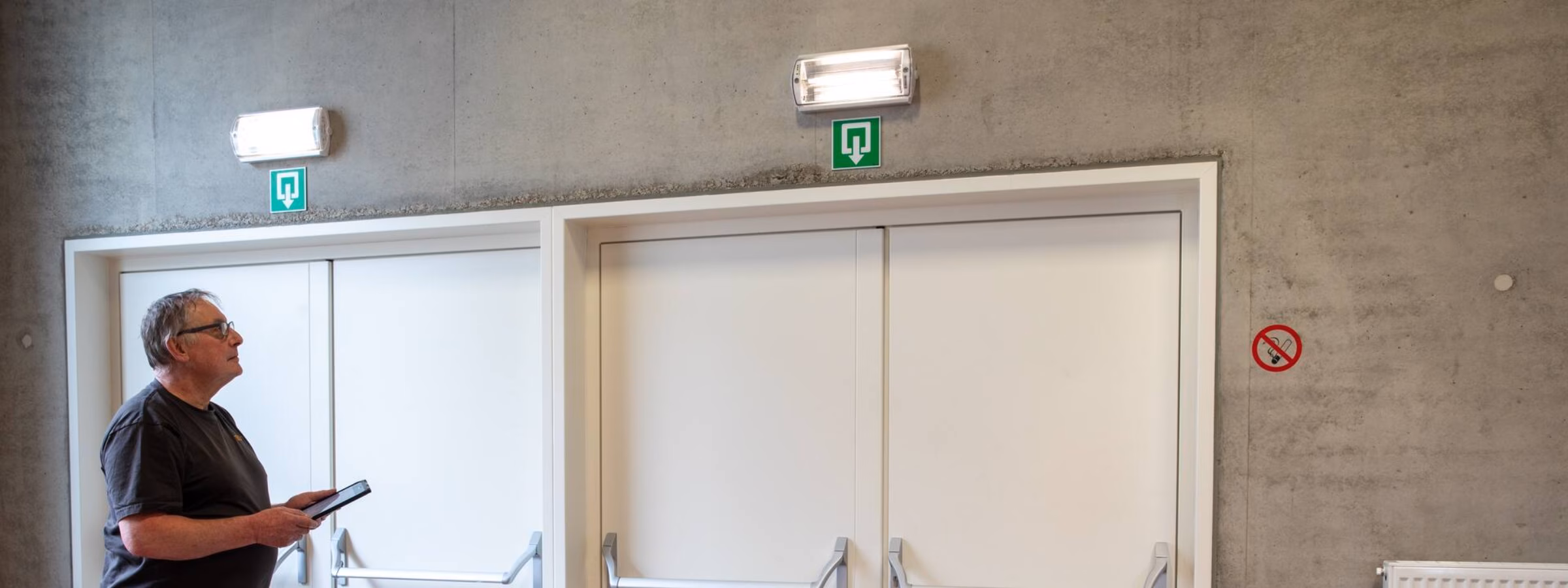 Inspecteur controleert nooddeuren en vluchtwegen in een gebouw met behulp van een tablet.