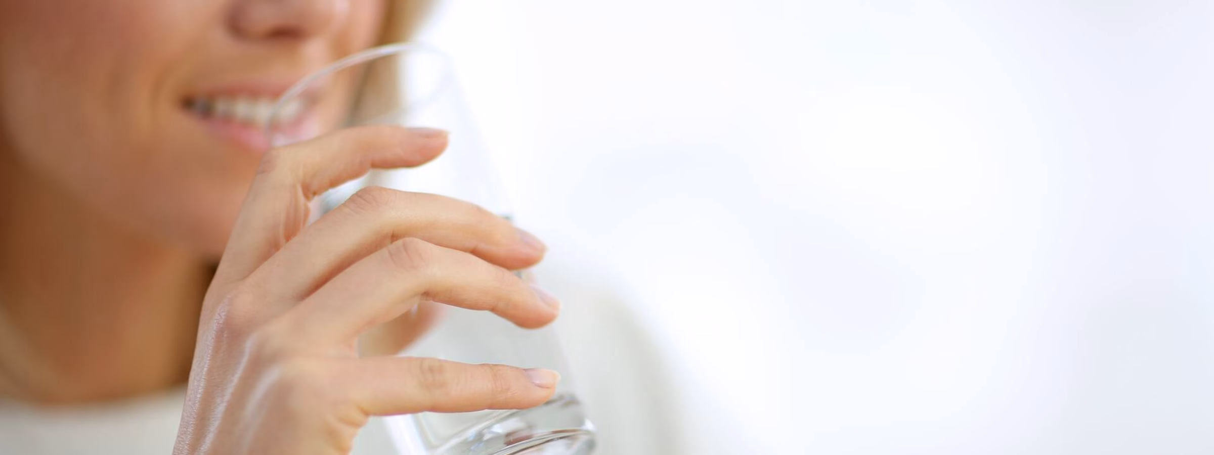 Une personne boit un verre d'eau dans un intérieur lumineux.