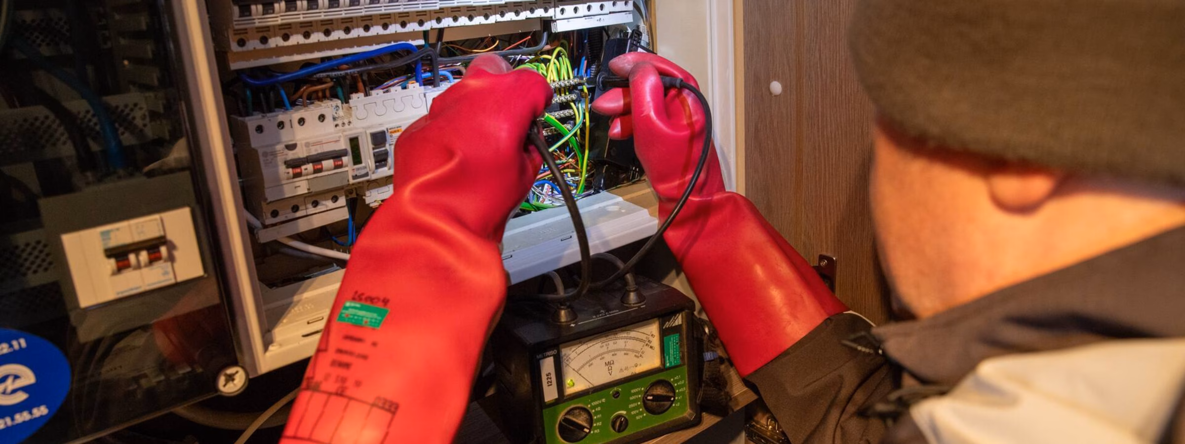 Ein Elektrotechniker führt mit Schutzhandschuhen eine Isolationswiderstandsmessung in einem Sicherungskasten durch.