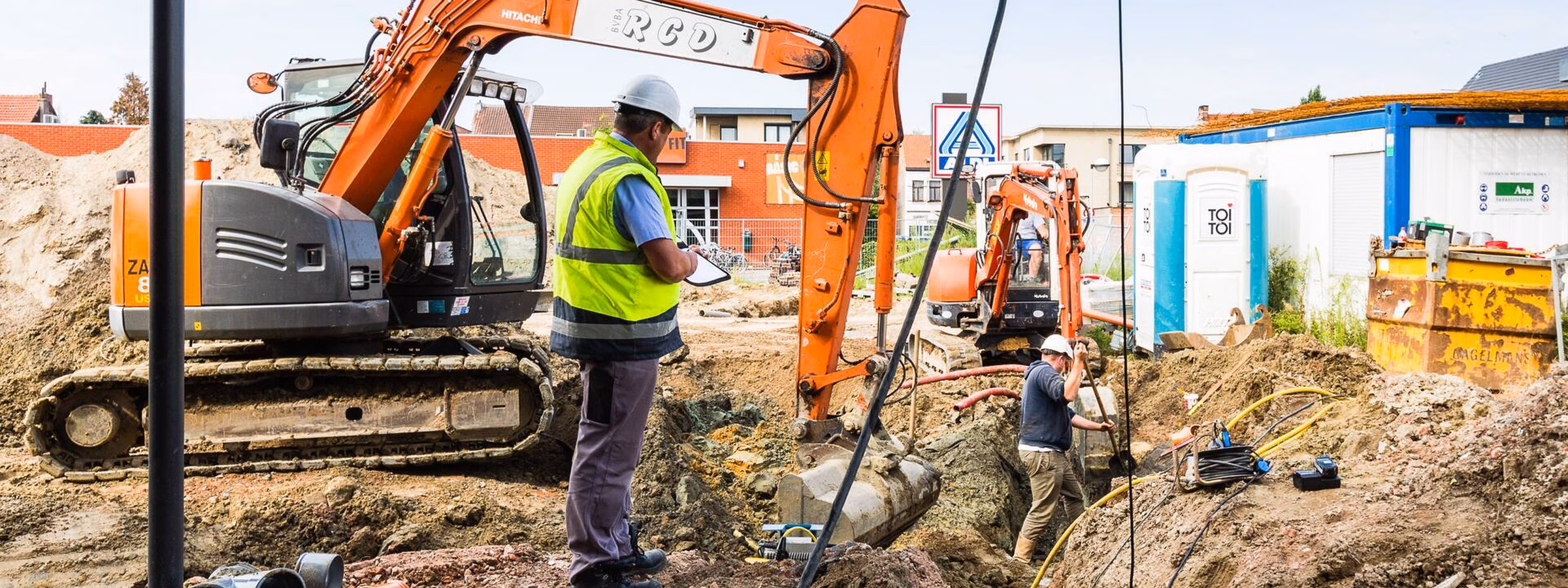 A technician supervises excavation work at a construction site involving excavators and underground infrastructure.