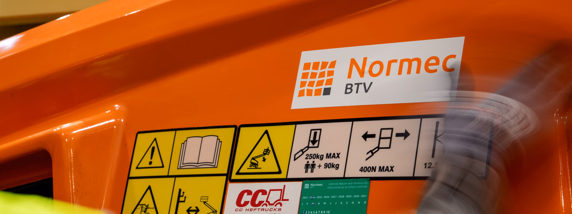 Detailfoto van veiligheidsstickers en Normec BTV-markering op een hoogwerker.