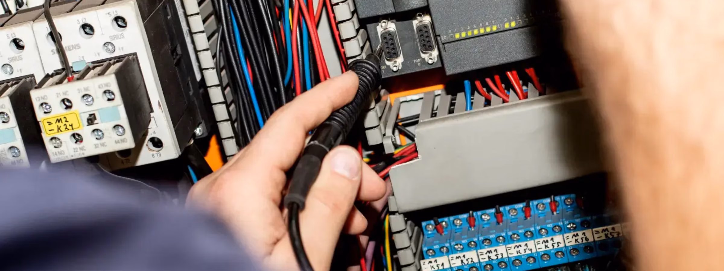 Ein Techniker führt Messungen in einem geöffneten Schaltschrank mit Verkabelung und Komponenten durch.