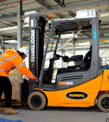 Warehouse employee wearing high-visibility safety clothing performs a pre-use inspection on a forklift in a modern industrial facility, highlighting operator training, workplace safety, equipment certification, compliance requirements, and safe material handling operations.