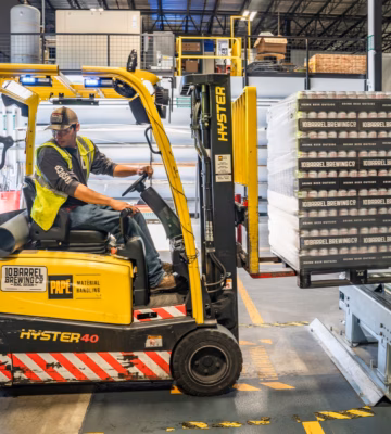 Een heftruckchauffeur transporteert goederen in een magazijn met industriële opslagstellingen.