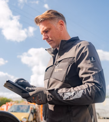 Un collaborateur vérifie des données sur une tablette sur un chantier, avec du matériel en arrière-plan