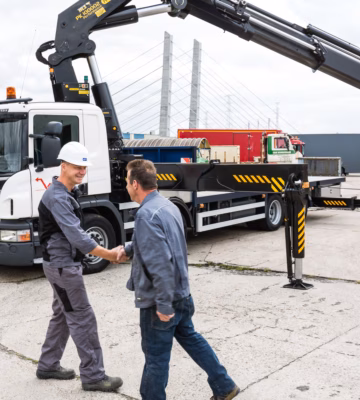 Twee medewerkers overleggen op een werkterrein naast een vrachtwagen met autolaadkraan.
