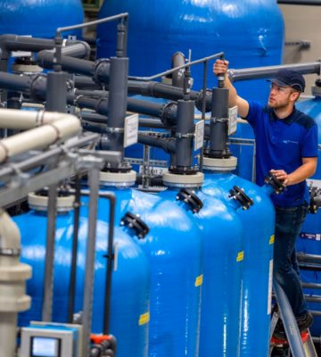 Un technicien effectue des travaux d'inspection et d'entretien sur une station d'épuration comprenant des canalisations et des bassins de filtration.