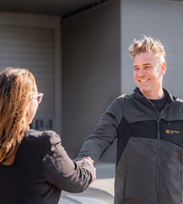 Twee personen begroeten elkaar op een bedrijfsterrein voor een bedrijfsgebouw.
