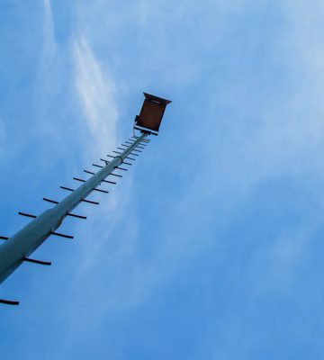 Een hoge mast met platform steekt af tegen een heldere blauwe lucht.
